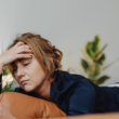 jonge vrouw ligt op de bank met mobiel in de hand en kijkt vermoeid