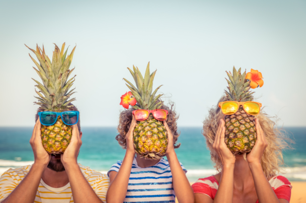 Drie mensen op vakantie die gezond bezig zijn. Ze hebben allemaal een ananas voor hun hoofd op het strand.