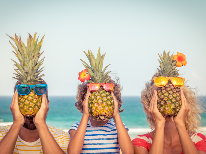 Drie mensen op vakantie die gezond bezig zijn. Ze hebben allemaal een ananas voor hun hoofd op het strand.
