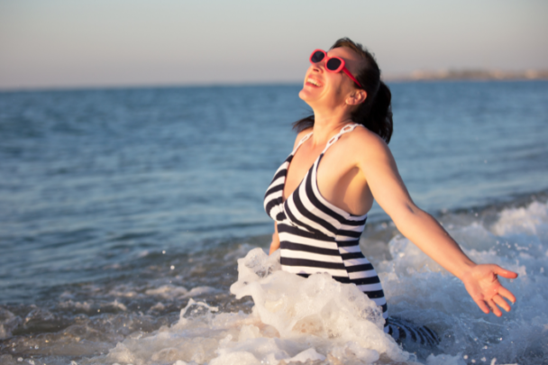 Vrouw in badpak staat vrolijk in de zee