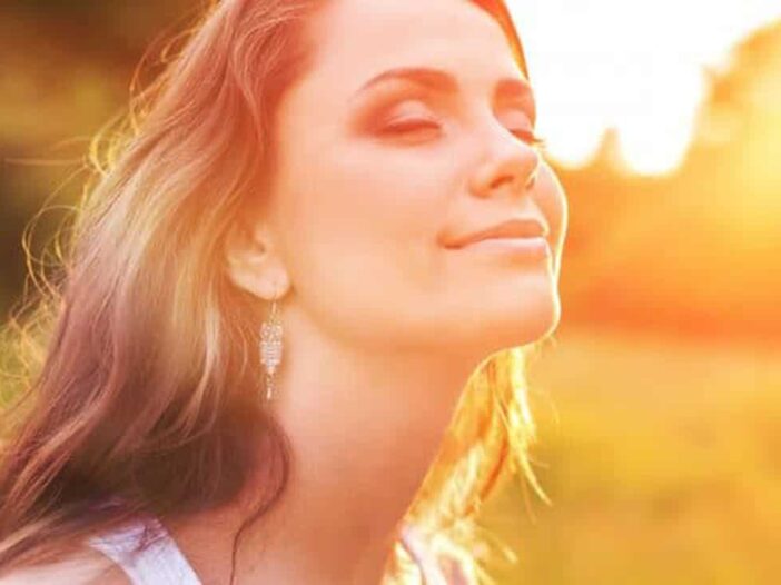 vrouw kijkt in de zon met gesloten ogen en oogt tevreden en blij|Young woman on field under sunset light|een houten tafel met twee dumbbells