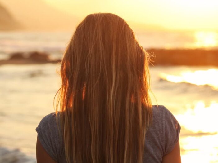 achteraanzicht van een vrouw die uitkijkt op de zee bij zonsondergang