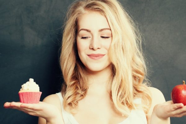 blonde vrouw met in de eene hand een cupcake en in de andere een appel