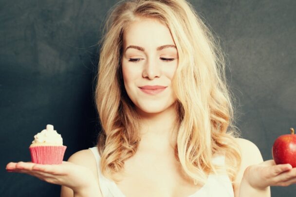 blonde vrouw met in de eene hand een cupcake en in de andere een appel