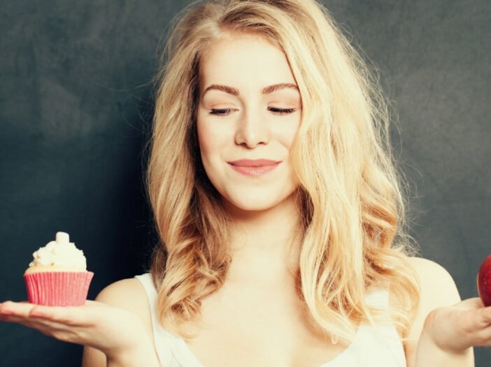 blonde vrouw met in de eene hand een cupcake en in de andere een appel