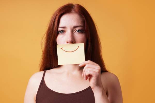 meisje met post-it met een glimlach er op getekend voor haar gezicht
