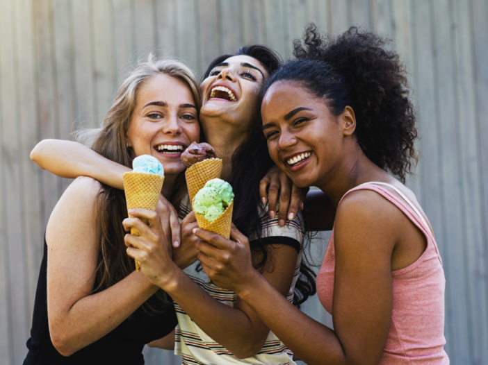 drie vrolijke vrouwen knuffelen elkaar en eten een ijsje|drie vriendinnen aan tafel