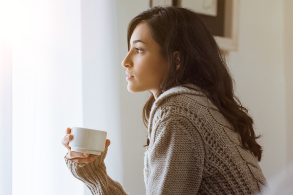 vrouw met kopje koffie kijkt uit haar raam