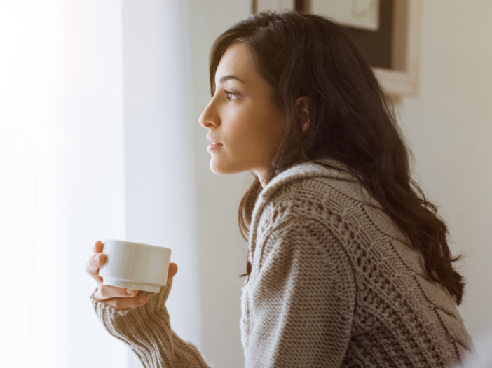 vrouw met kopje koffie kijkt uit haar raam