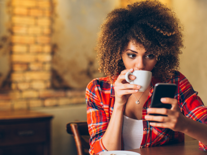 vrouw drinkt koffie en gebruikt haar smartphone
