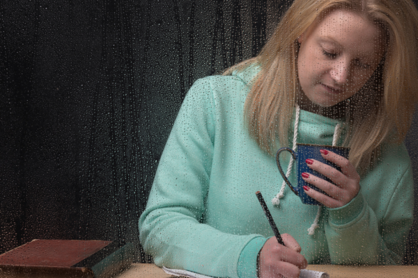 vrouw doet een schrijfoefening en drinkt thee|vrouw doet een schrijfoefening en drinkt thee