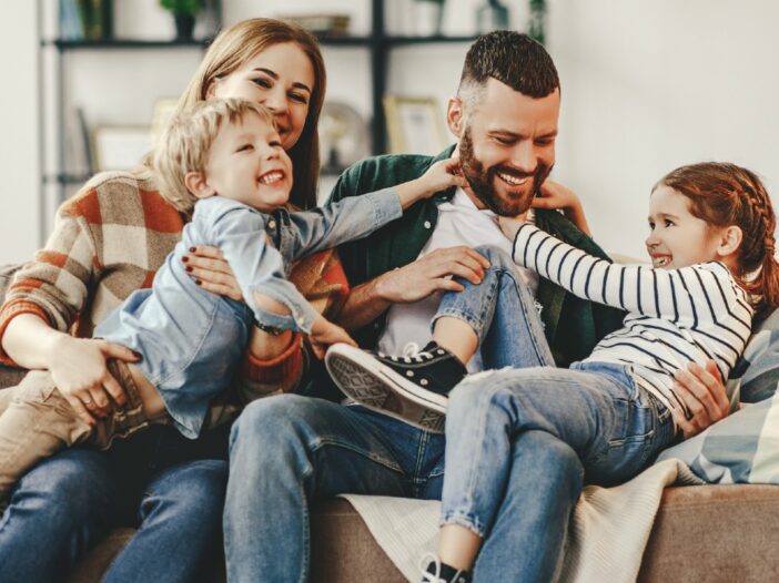 gezin van man en vrouw plus twee kinderen op de bank aan het stoeien|banner over ouderschap: foto's van gezinnen met in blauw tekstvak de tekst 'over ouderschap'