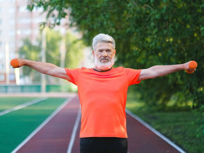 Man met twee dumbbells staat op spotveld