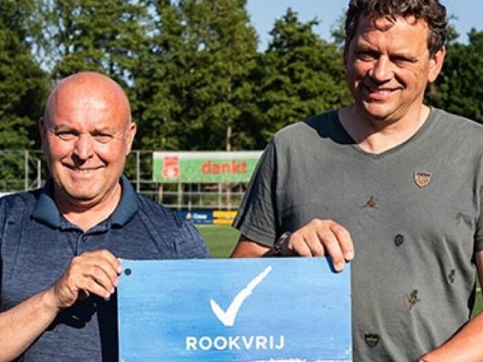 Twee mannen op een sportveld houden een bord vast met daarop een vinkje en de tekst rookvrije generatie