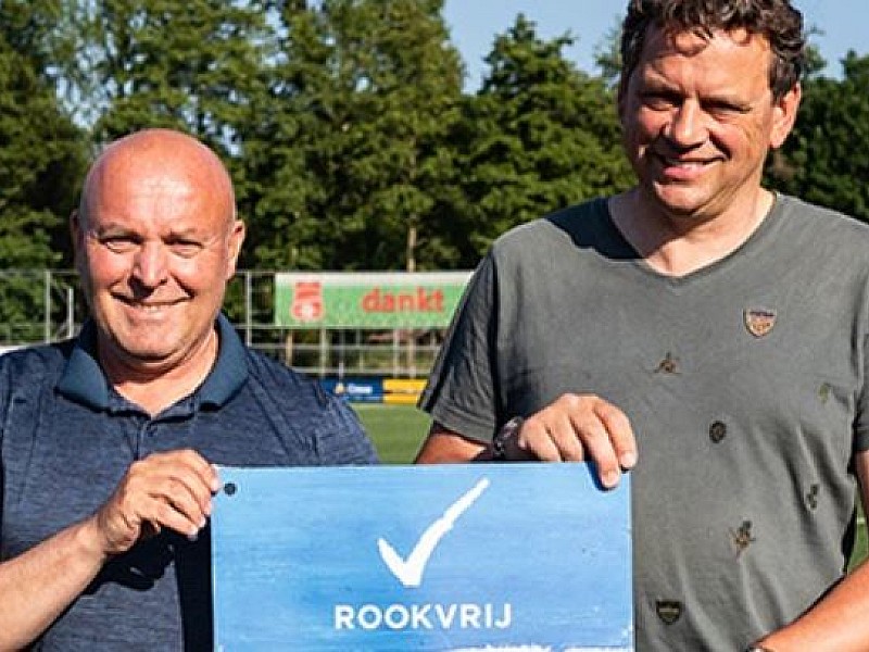 Twee mannen op een sportveld houden een bord vast met daarop een vinkje en de tekst rookvrije generatie