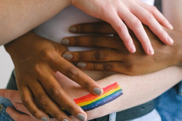 handen houden elkaar vast met in beeld een kleine regenboog vlag