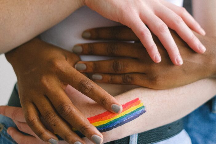 handen houden elkaar vast met in beeld een kleine regenboog vlag