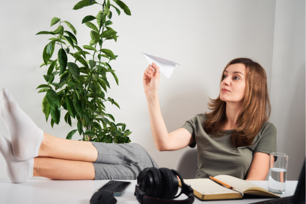 vrouw zit aan bureau en gooit een papieren vliegtuigje