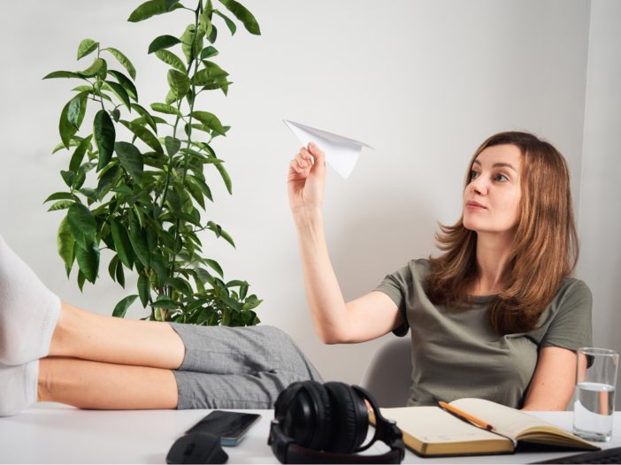 vrouw zit aan bureau en gooit een papieren vliegtuigje