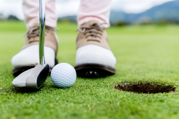 twee voeten en golfclub bij een golf hole