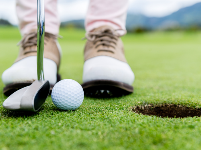 twee voeten en golfclub bij een golf hole