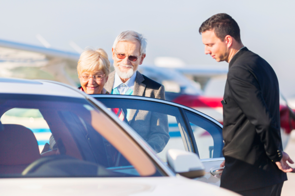 twee ouderen stappen in de auto bij een chauffeur