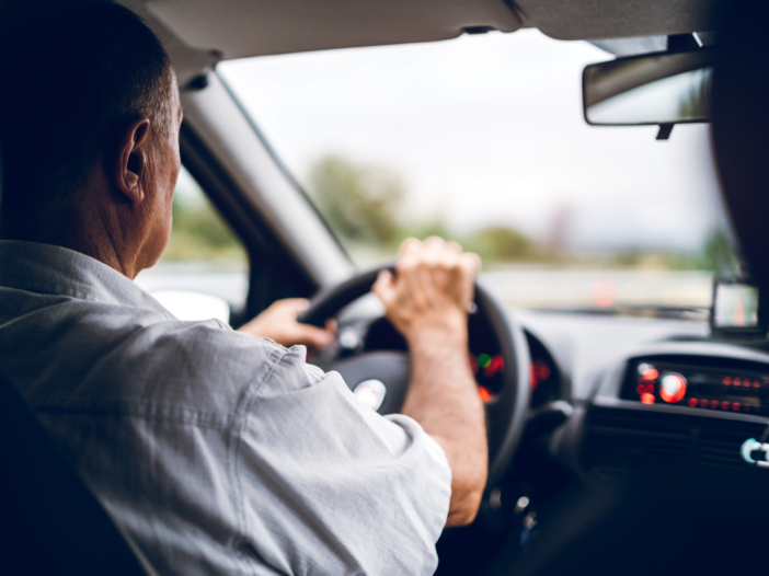 oudere man zit achter het stuur van een auto