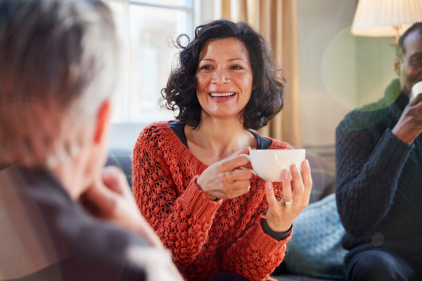 Drie mensen drinken samen een kopje koffie. De vrouw moet ook lachen daarbij.