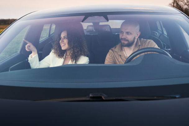 Twee mensen in een auto. Een man en een vrouw, ze lachen allebei terwijl ze naar hetzelfde kijken.