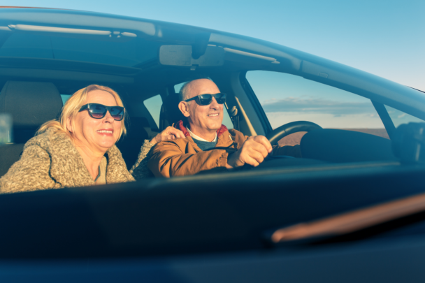 Twee lachende mensen in een auto samen. De zon schijnt en de man is de chauffeur van de vrouw.