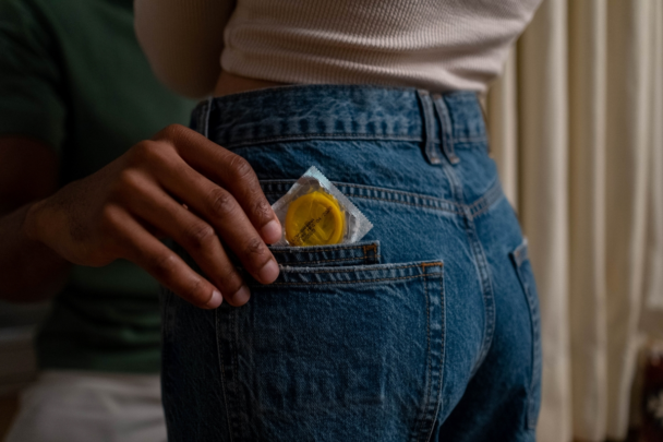 Hand van een man haalt een condoom uit de kontzak van de spijkerbroek van een vrouw
