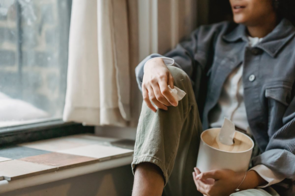 een vrouw staart uit haar raam en houdt een tissue vast in haar hand