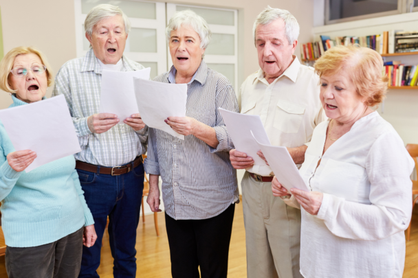 Vijf ouderen met een blaadje in hun hand die aan het zingen zijn.