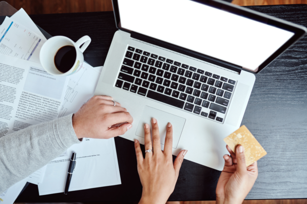 Man en vrouw zitten samen achter de laptop. De vrouw heeft een geldbriefje in haar hand en ze zijn samen de geldzaken aan het regelen en bekijken.