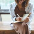 Vrouw lacht en schrijft blij in een notitieboek