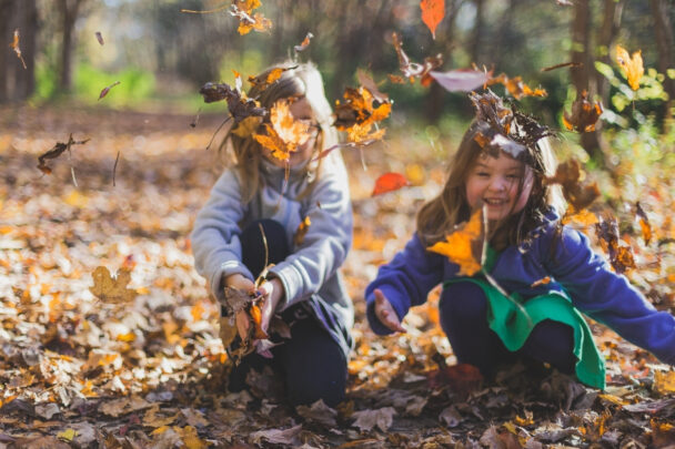 Twee meisjes spelen buiten in herfstbladeren.