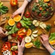 Vijf handen reiken naar een plateau met allerlei gezond, kleurrijk voedsel erop.