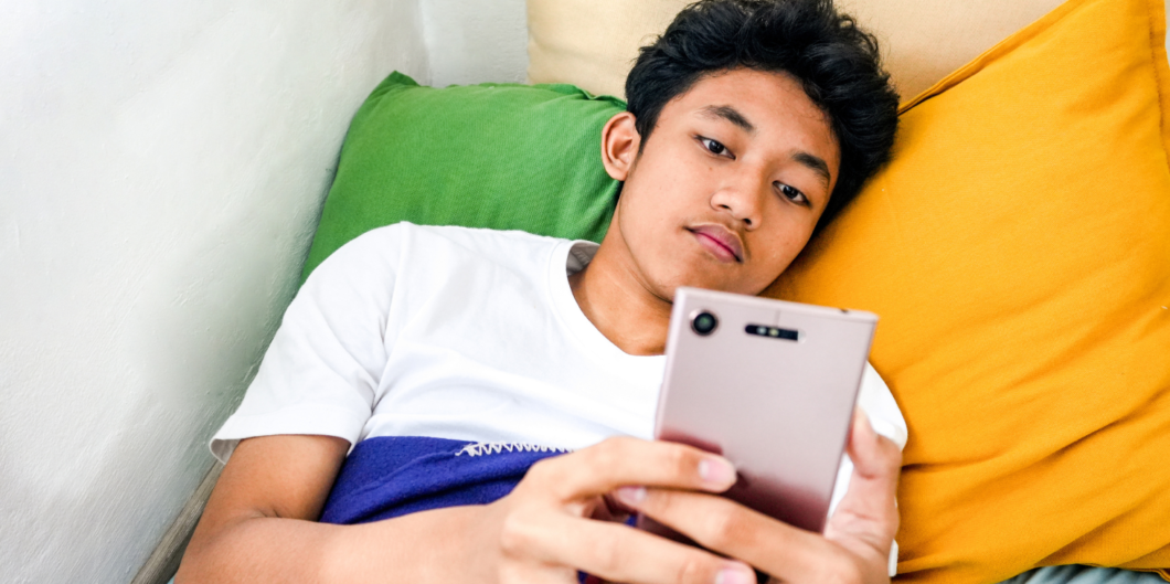 Jongen ligt in bed te scrollen op mijn mobiel