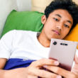 Jongen ligt in bed te scrollen op mijn mobiel