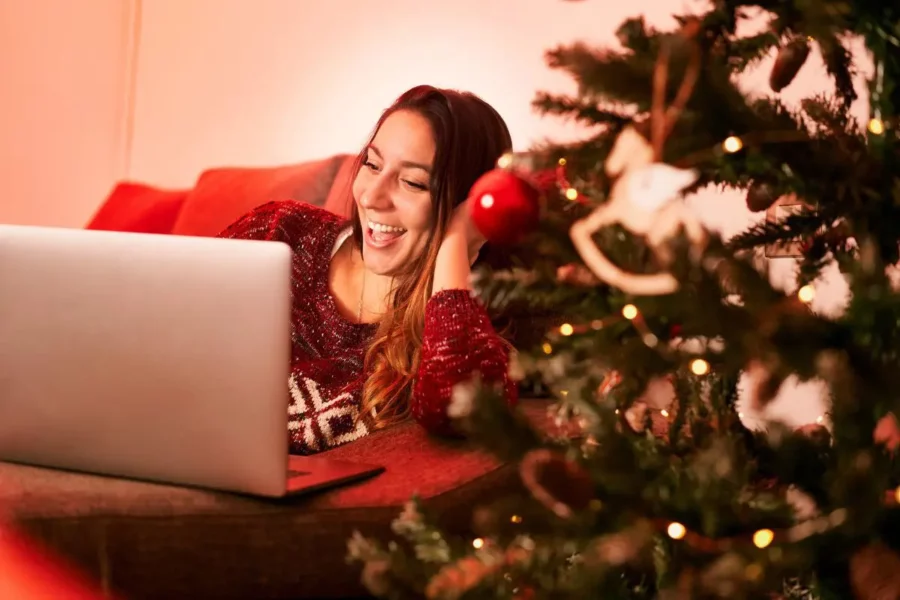 Vrouw ligt op de bank en gebruikt haar laptop. Naast haar staat de kerstboom.