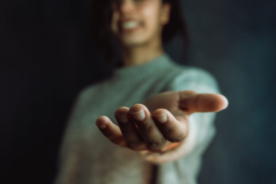 Vrouwenhand reikt naar de camera. Vrouw staat er breed glimlachend bij.