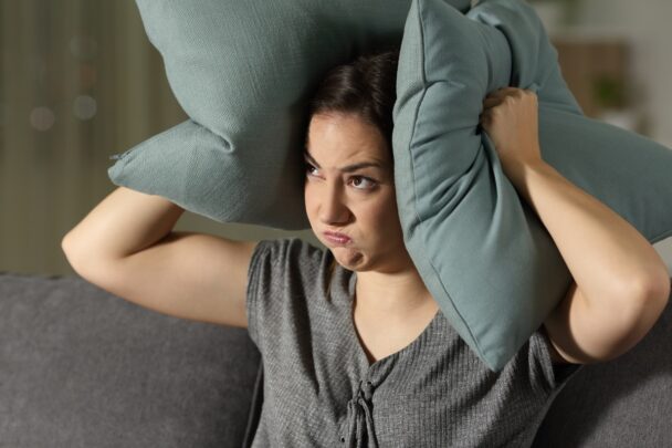 Vrouw drukt geïrriteerd een kussen tegen haar oren.