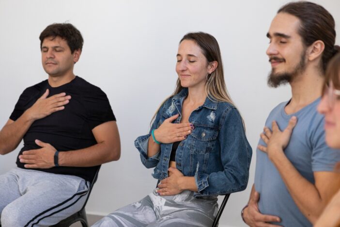Twee mannen en een vrouw zijn aan het mediteren op een stoel.