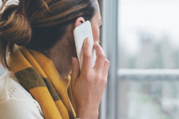 Vrouw telefoneert en kijkt uit raam.