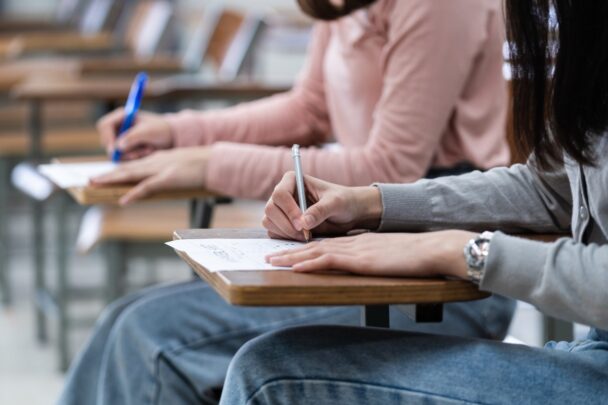 Twee tieners zitten aan een schooltafeltje een toets te maken.
