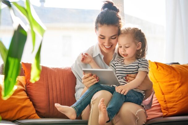 Moeder met kind op schoot kijkt naar tablet met kind samen.