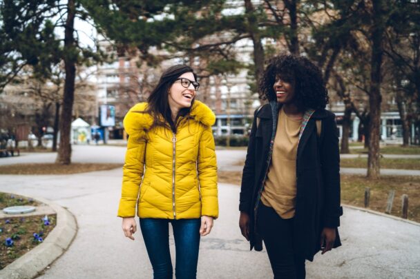 Twee jonge vrouwen wandelen samen door park.