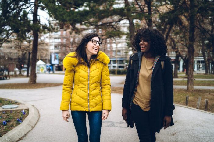 Twee jonge vrouwen wandelen samen door park.