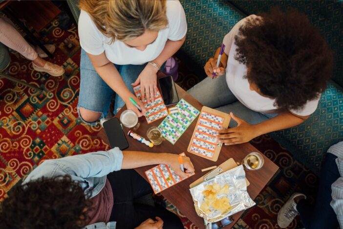 Bovenaanzicht van drie vrouwen die bingo spelen op papieren bingokaarten.