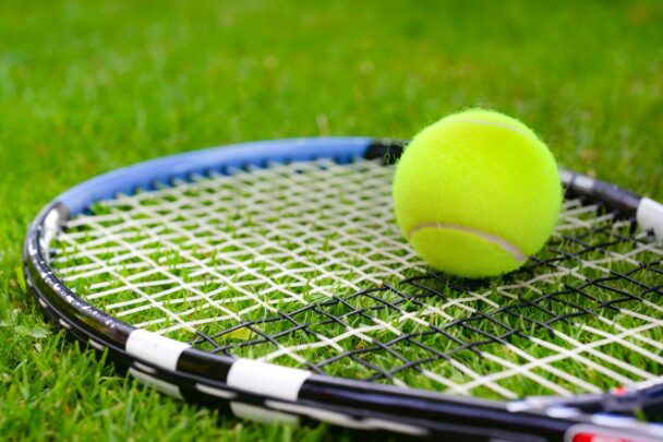 Tennisbal ligt op een tennisracket in het gras.